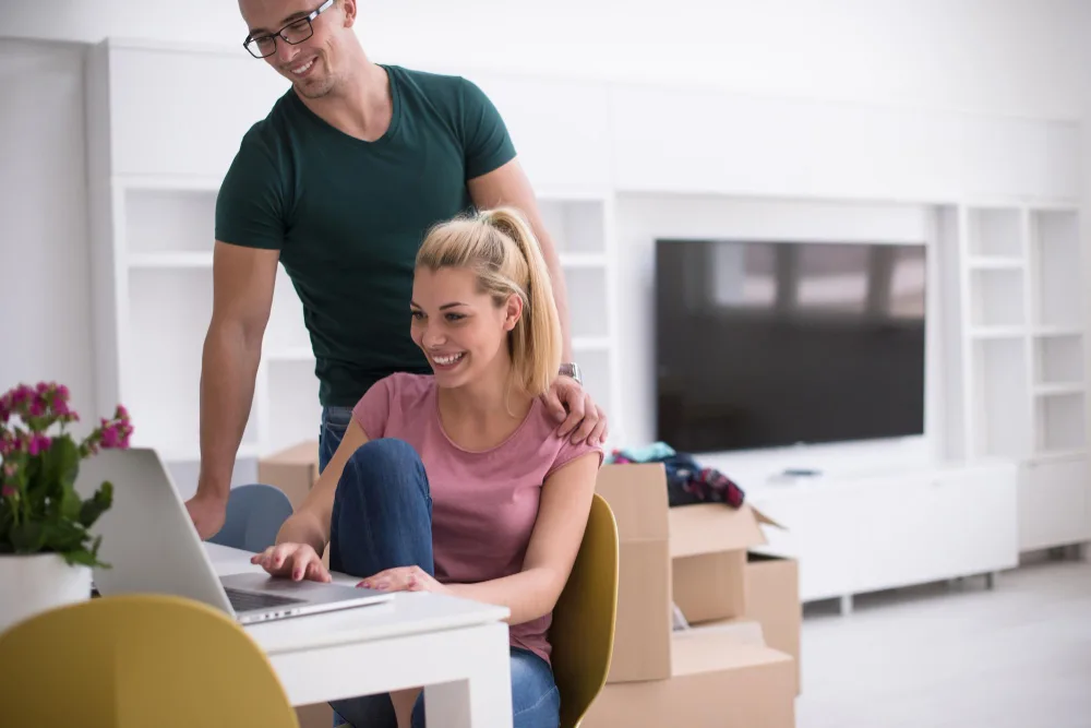 young-couple-moving-new-home-man-woman-table-using-notebook-laptop-computer-plans-with-boxes-around-them